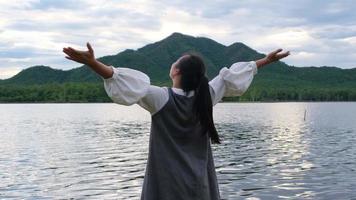 asiatische Frau, die bei Sonnenuntergang die Aussicht auf die Natur am See genießt. Lifestyle- und Urlaubsreisekonzept video