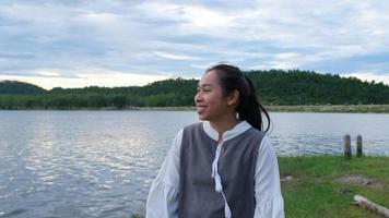 mujer asiática disfrutando de la vista de la naturaleza junto al lago al atardecer. estilo de vida y concepto de viaje de vacaciones video