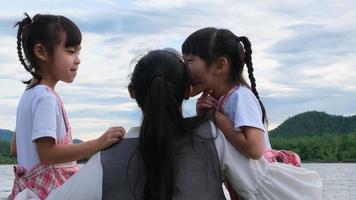 Happy mother hugging her cute little sisters enjoying the nature by the lake. Happy family, mother and her daughters playing feeling happy in the park. video