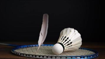 imagem em câmera lenta de penas caindo na raquete com bolas de badminton em fundo preto, conceito de evento esportivo de peteca. video