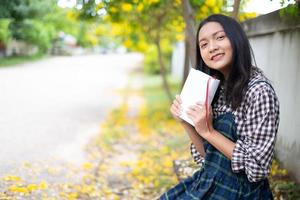 Young girl sitting on a bench reading a book under a beautiful tree. photo