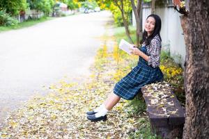 Young girl sitting on a bench reading a book under a beautiful tree. photo