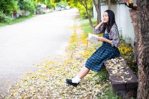 niña sentada en un banco leyendo un libro bajo un hermoso árbol. foto