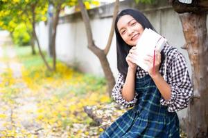 Young girl sitting on a bench reading a book under a beautiful tree. photo