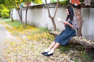 Young girl sitting on a bench reading a book under a beautiful tree. photo