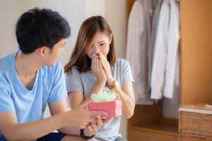 Beautiful young asian couple in love surprise gift box in bedroom at home, family anniversary with enjoy and romantic together wife and husband with relationship, Celebrating Valentine Day concept. photo