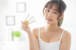 Beautiful portrait young asian woman holding and presenting cream or lotion product, beauty asia girl show cosmetic makeup and moisturizing for skin care, healthy care and wellness concept. photo