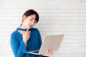 hermosa mujer joven asiática hipster usando una idea de pensamiento portátil de trabajo sobre fondo de hormigón de cemento, duda de chica y pregunta con internet de computadora en línea, concepto independiente y de negocios. foto