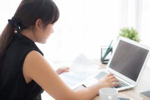 Young asian woman working and typing with laptop computer at office, businesswoman looking graph diagram analysis statistic data of finance, girl using notebook, profit growth, business concept. photo