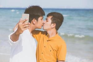 Gay portrait young couple smiling taking a selfie photo together with smart mobile phone at beach, LGBT homosexual lover with kiss in the vacation at sea, two man going to travel, holiday concept.