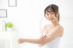 Beautiful portrait young asian woman smile applying sunscreen cream or lotion on skin care at bedroom, beauty asia girl using makeup and cosmetic for smooth and silky, wellness and health concept. photo