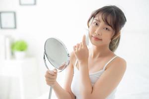 Beautiful young asian woman smile and joy with skin care use oil blotting paper on face looking mirror in the room, beauty asia girl happy and cheer makeup and cosmetic, health care on facial concept. photo