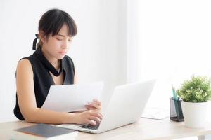 Young asian woman working and typing with laptop computer at office, businesswoman looking graph diagram analysis statistic data of finance, girl using notebook, profit growth, business concept. photo
