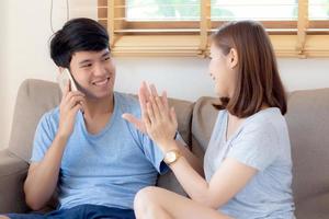 hermosa joven pareja asiática hombre y mujer gesto alto cinco juntos mientras el hombre habla teléfono móvil inteligente en el sofá, celebración familiar disfruta y emocionado con feliz en el sofá, concepto de estilo de vida. foto