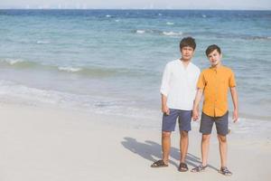 retrato homosexual joven pareja asiática de pie juntos en la playa en verano, asia gay tomados de la mano yendo al mar por placer y relajarse con romántico y feliz en vacaciones en el mar, lgbt con concepto legal. foto