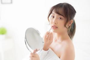 hermoso retrato joven mujer asiática mirando espejo aplicando lápiz labial de maquillaje en la habitación, labios de belleza maquillaje de niña de asia y moda cosmética en la boca en casa, estilo de vida y concepto de atención médica. foto