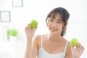 hermoso retrato joven mujer asiática sosteniendo y comiendo fruta de manzana verde en el dormitorio en casa, estilo de vida de nutrición niña saludable y cuidado concepto de pérdida de peso, salud y bienestar. foto