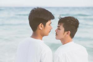 Back view young asian couple standing together on beach in summer, asia gay holding hands going sea for leisure and relax with romantic and happy in vacation at sea, LGBT with legal concept. photo