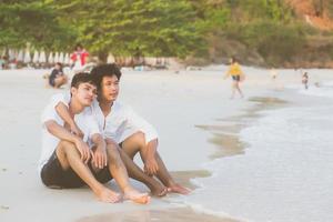 retrato homosexual joven pareja asiática sentada abrazada en la playa en verano, turismo gay de asia para el ocio y relajarse con romanticismo y felicidad en vacaciones en el mar, concepto legal lgbt. foto