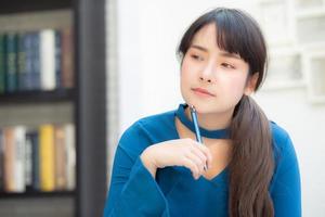 hermosa joven escritora asiática sonriendo pensando en una idea y escribiendo en un cuaderno o diario con feliz estilo de vida de una chica asiática es estudiante, planificación femenina de trabajo, educación y concepto de negocios. foto