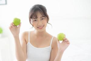 hermoso retrato joven mujer asiática sosteniendo y comiendo fruta de manzana verde en el dormitorio en casa, estilo de vida de nutrición niña saludable y cuidado concepto de pérdida de peso, salud y bienestar. foto