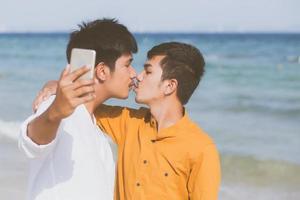 Gay portrait young couple smiling taking a selfie photo together with smart mobile phone at beach, LGBT homosexual lover with kiss in the vacation at sea, two man going to travel, holiday concept.