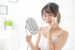 Beautiful young asian woman smile and joy with skin care use oil blotting paper on face looking mirror in the room, beauty asia girl happy and cheer makeup and cosmetic, health care on facial concept. photo