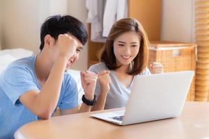 Beautiful portrait young asian couple working laptop with smile and happy sitting in bedroom, man and woman using notebook computer with excited and satisfied, business and success concept. photo