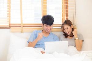 Beautiful portrait young asian couple working laptop with smile and happy sitting in bedroom, man and woman using notebook computer with excited and satisfied, business and success concept. photo