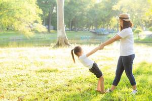 Young asian mother and little daughter playing the park with fun and happiness, family enjoy and relax and leisure together, mom and children smiling laughing in summer day. photo