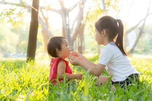 hermoso niño asiático joven sentado jugando en verano en el parque con disfrute y alegre en la hierba verde, actividad infantil con relajación y felicidad juntos en el concepto de pradera, familia y vacaciones. foto