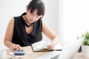 hermosa joven asiática calculando los gastos del hogar y escribiendo un cuaderno en el escritorio, niña revisando la factura y el estrés y la nota, la mujer se preocupa por la deuda y el concepto de impuestos, finanzas y negocios. foto