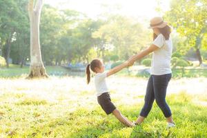 Young asian mother and little daughter playing the park with fun and happiness, family enjoy and relax and leisure together, mom and children smiling laughing in summer day. photo