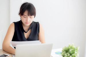 Young asian woman working and typing with laptop computer at office, businesswoman looking graph diagram analysis statistic data of finance, girl using notebook, profit growth, business concept. photo