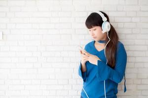 hermoso retrato mujer joven asiática de pie feliz disfrutar y divertirse escuchar música con auriculares sobre fondo de hormigón de cemento, estilo de vida de chica relajar radio de sonido con auriculares, concepto de tecnología. foto