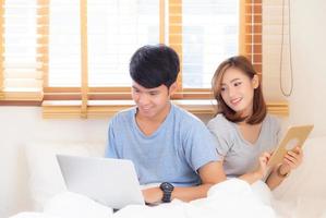 Beautiful young asian couple cheerful freelance working with man using laptop and woman using tablet on couch, family relax and sharing communication together at home, lifestyle concept. photo