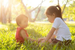 Beautiful young asian kid sitting playing in summer in the park with enjoy and cheerful on green grass, children activity with relax and happiness together on meadow, family and holiday concept. photo