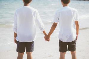 Asian gay couple holding hands together on the beach with relax and leisure in summer, LGBT homosexual legal two man happy and romantic in vacation, relationship sex lover concept. photo