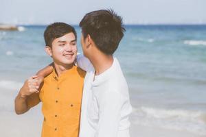 retrato homosexual joven pareja asiática de pie abrazo juntos en la playa en verano, turismo gay de asia para el ocio y relajarse con romanticismo y felicidad en vacaciones en el mar, concepto lgbt. foto