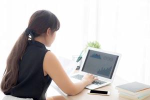 Young asian woman working and typing with laptop computer at office, businesswoman looking graph diagram analysis statistic data of finance, girl using notebook, profit growth, business concept. photo
