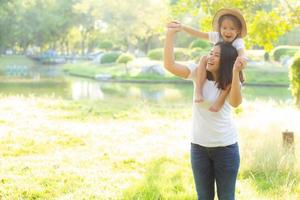 Beautiful young asian mother carrying little daughter with smile, child ride the neck on mom with happiness and cheerful together in the park, lifestyle family with enjoy and fun concept. photo