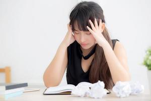 Beautiful asian woman tired and stressed with writing overworked at desk, girl with worried not idea with notebook and crumpled paper at office, freelance and business concept. photo