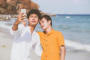 retrato gay pareja joven sonriendo tomando una foto selfie junto con un teléfono móvil inteligente en la playa, amante homosexual lgbt en las vacaciones en el mar, dos hombres van a viajar, concepto de vacaciones.