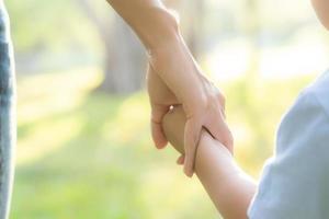 Closeup mother or parent and son holding hand with love together in summer outside in the park, mom take care kid holding palm with affection, child have a trust for mother, family concept. photo