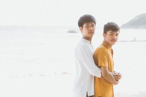 retrato homosexual joven pareja asiática de pie abrazo juntos en la playa en verano, turismo gay de asia para el ocio y relajarse con romanticismo y felicidad en vacaciones en el mar, concepto lgbt. foto