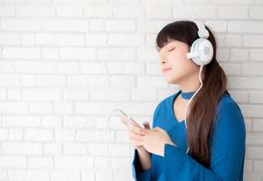 hermoso retrato mujer joven asiática de pie feliz disfrutar y divertirse escuchar música con auriculares sobre fondo de hormigón de cemento, estilo de vida de chica relajar radio de sonido con auriculares, concepto de tecnología. foto