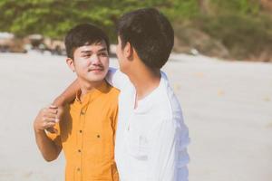 retrato homosexual joven pareja asiática de pie abrazo juntos en la playa en verano, turismo gay de asia para el ocio y relajarse con romanticismo y felicidad en vacaciones en el mar, concepto lgbt. foto