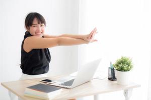 Beautiful young asian woman stretching muscle arms after working with laptop for protect office syndrome with relax, asia girl leisure and exercise because tired, business and healthy concept. photo