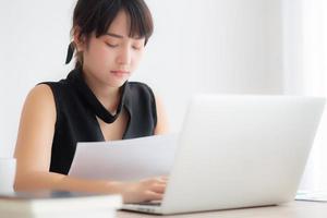Young asian woman working and typing with laptop computer at office, businesswoman looking graph diagram analysis statistic data of finance, girl using notebook, profit growth, business concept. photo