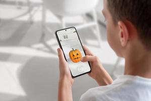 Boy on a mobile phone is playing an augmented reality game. View over shoulder at the phone display. Pumpkin throwing game concept photo